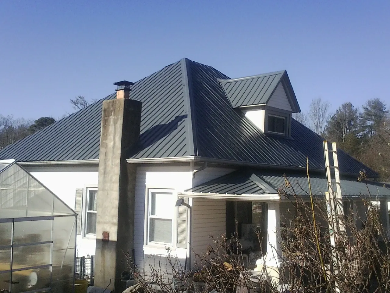 Dark blue standing seam metal roof on a white farmhouse with dormer — Slate & Tile Roof Repair by Roofing Brothers in Hassell