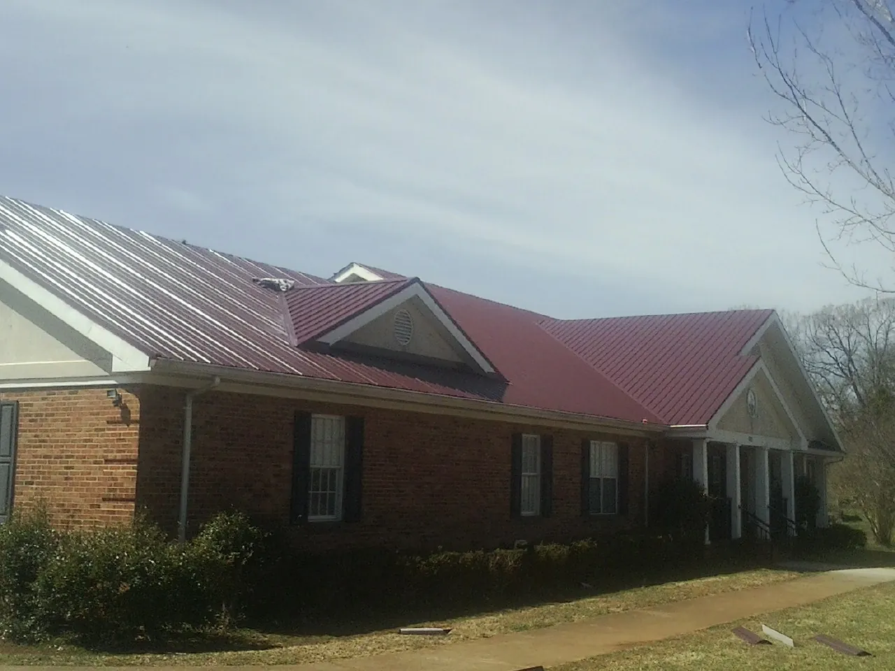 Red metal roof with gabled entries on a long brick building, from a Hail Damage Roof Repair job in Hassell