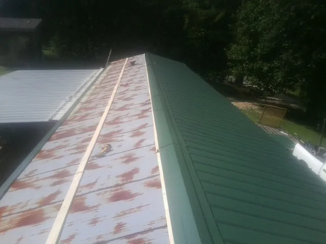 Old rusted panels beside newly installed green metal roofing — Wind Damage Roof Repair by Roofing Brothers in Hassell