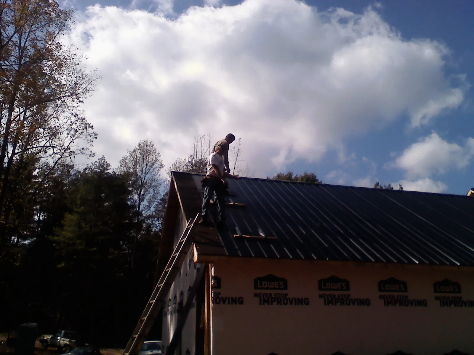 Roofer fastening dark metal panels high against a cloudy sky, from a Roof Inspection job in Hassell