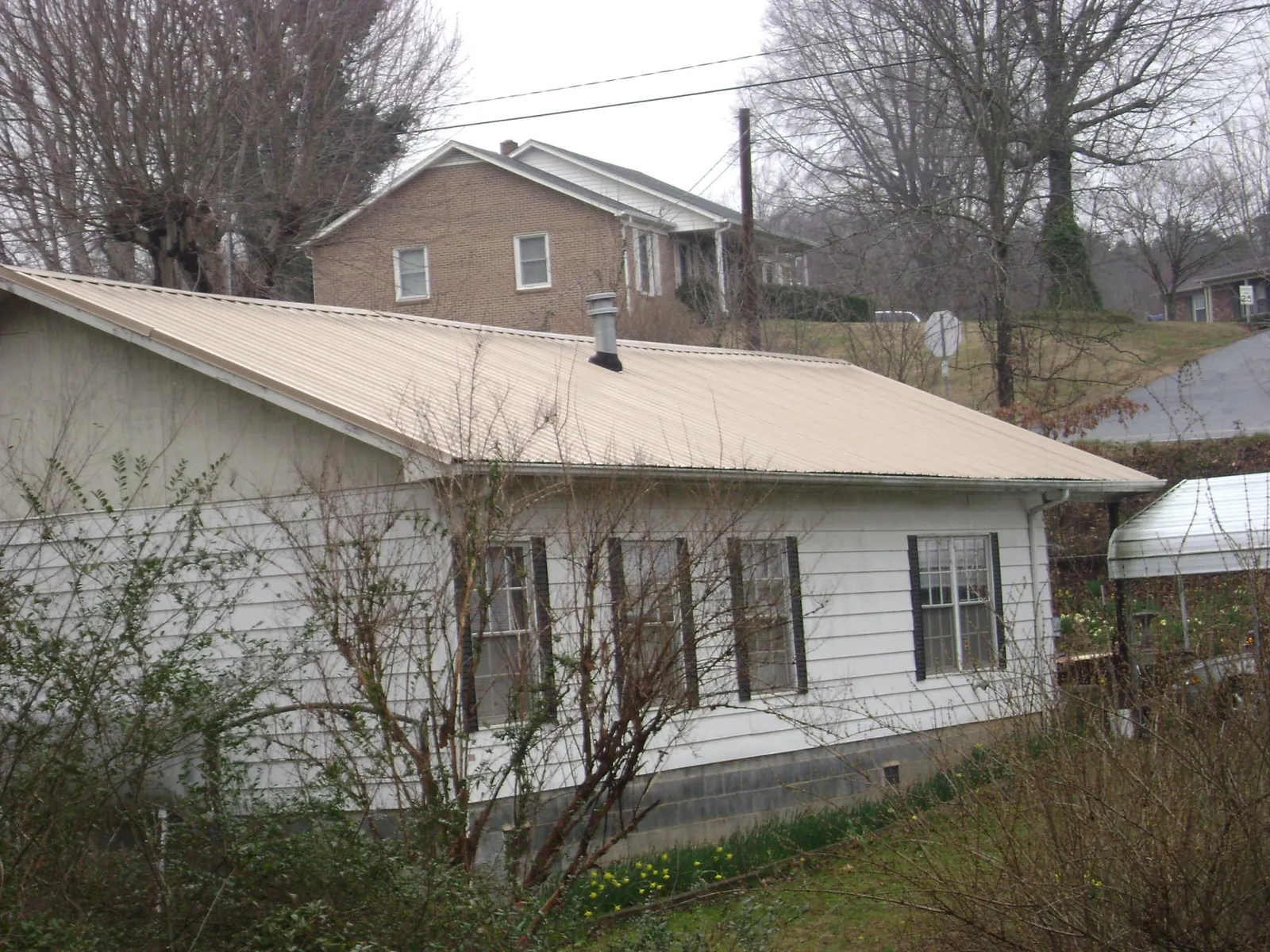 Tan metal roof on a white sided house set into a hillside — Commercial Roofing by Roofing Brothers in Hassell